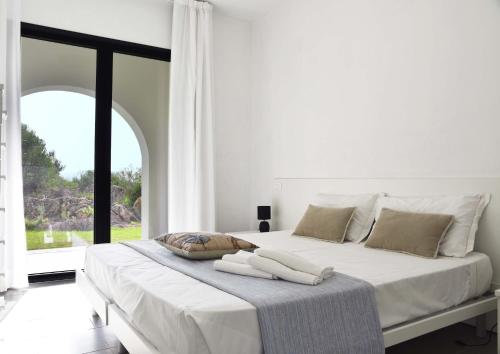 a white bedroom with a large bed with a window at Geovillage Green Residence in Olbia