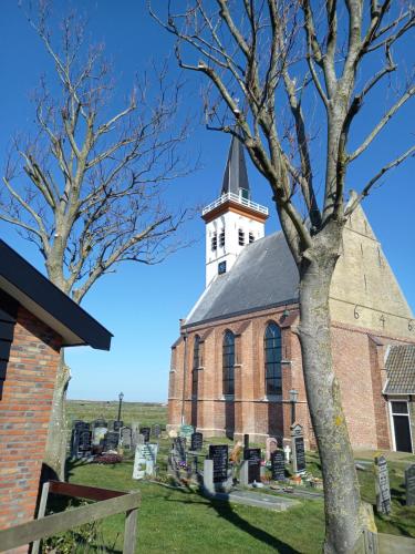 an old brick church with a steeple and a tree at B&B kamers en meer Het Spookhuis in Den Hoorn