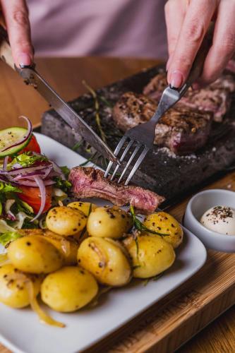 a person cutting a plate of food with a steak and potatoes at ibis Styles Lublin Stare Miasto in Lublin