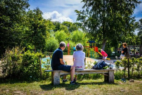 un homme et une femme assis sur un banc devant une aire de jeux dans l'établissement Holidayhome - Kon Emmaweg 26 - Vrouwenpolder - Uitspanning Oranjezon, à Vrouwenpolder