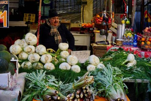 a woman standing in a market with a pile of vegetables at Il mare in un bicchiere in Sciacca