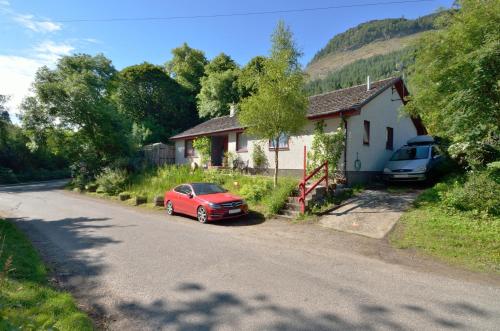 a red car parked next to a house on a road at The Bridge Suite in Invermoriston