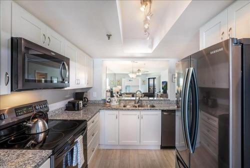 a kitchen with white cabinets and a black refrigerator at Gulf Watch 204 Condo in Bradenton Beach