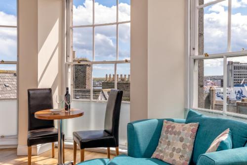 a living room with a blue couch and a table and windows at Victoria Court Suites - Aberdeen in Aberdeen