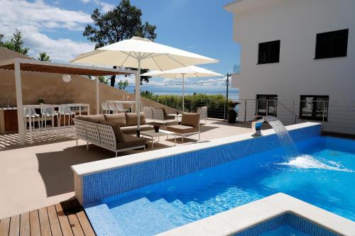 uma piscina com cadeiras e um guarda-sol ao lado de um edifício em MODENA MARIS-heated pool-grill-relax-jacuzzi apartments em Ičići