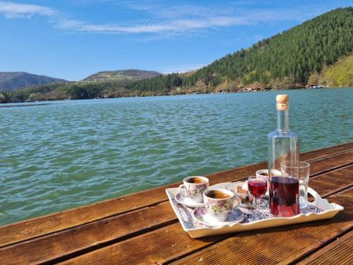 a tray with a bottle of wine and two cups on a table by a lake at Kućica na Jezeru Ovčarsko-kablarska klisura Boat Access Only in Čačak