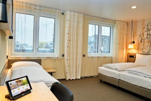 a hotel room with two beds and a desk and windows at McDreams Hotel München-Airport in Eching