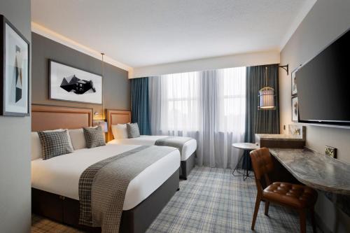 a hotel room with two beds and a desk at Leonardo Royal Hotel Edinburgh in Edinburgh