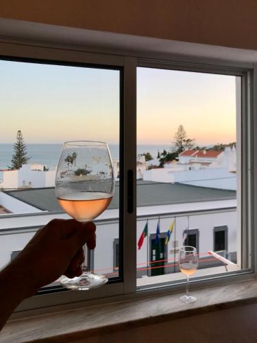a person holding a glass of wine in front of a window at Sea Light Seaview Vista Mar Apartment - Luz, Lagos in Luz