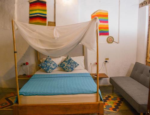 a bed with a canopy in a room with a couch at Pueblito Magico Hostel - Mompox in Mompos