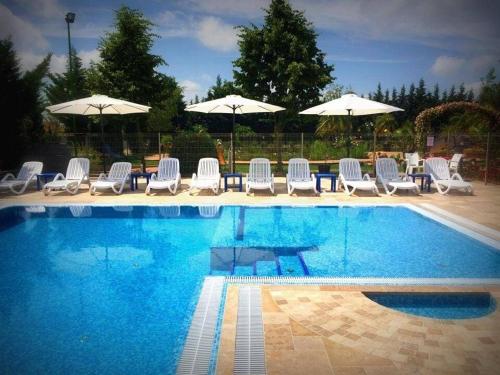a swimming pool with white chairs and umbrellas at Bagolyvár Inárcs in Inárcs