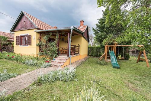 una pequeña casa amarilla con parque infantil en el patio en Csavargó Tanya, en Szalafő