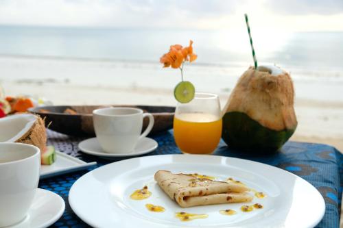 a table with a plate of food and a glass of orange juice at Sharazad Boutique Hotel in Jambiani