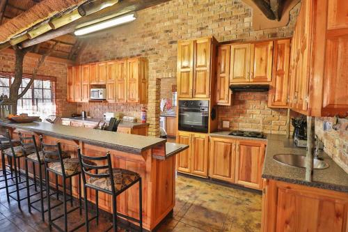 una cocina con armarios de madera y un bar con taburetes en Adventure Bush House, en Marloth Park