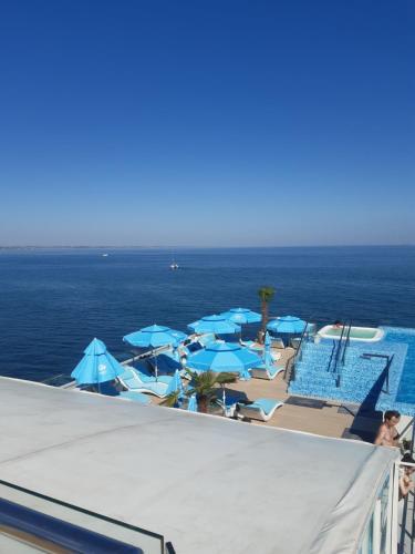 Una piscina con sombrillas azules y el océano. en London Apartment, Odessa, en Odessa