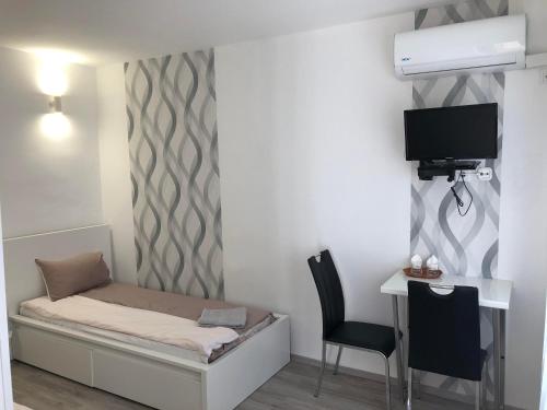 Habitación pequeña con cama, escritorio y TV. en Palma Vendégház, en Szeged