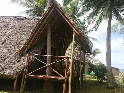 a hut with a thatched roof and palm trees at COCO REEF ECOLODGE in Kizimkazi