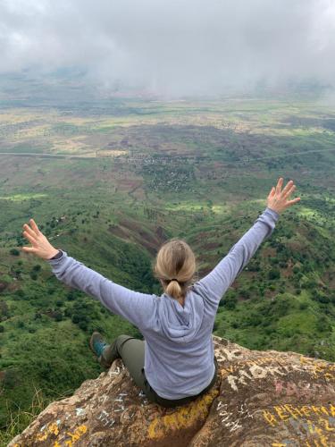 a woman sitting on top of a rock with her arms outstretched at David Crater Homestay in Lushoto