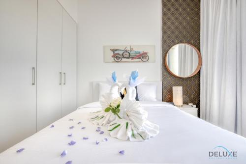 a white bed with a flower arrangement on it at Charismatic 1BR at UNA Town Square Dubailand by Deluxe Holiday Homes in Dubai