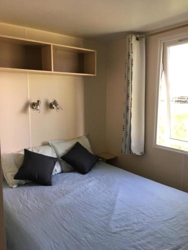 1 dormitorio con 1 cama con 2 almohadas y ventana en Mobil Home pour 6 personnes climatisé à quelques minutes des plages en Agde