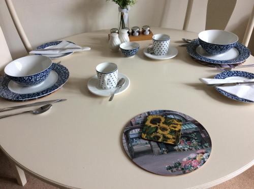 Rye Flatt Bed and Breakfast في كولن: طاولة بيضاء مع أكواب وصحون زرقاء وبيضاء