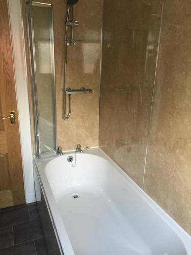 uma banheira branca com uma porta de duche envidraçada em Erradill Cottage em Southend