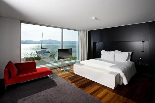 a bedroom with a bed and a red chair and a window at Altis Belem Hotel & Spa, a Member of Design Hotels in Lisbon