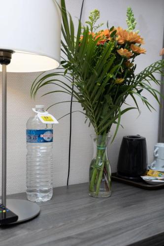 a vase of flowers on a table next to a bottle of water at Logis-Hôtel & Restaurant LE CARNOT in Bolbec