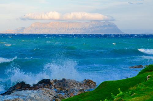 a wave in the ocean with a mountain in the background at casavacanza golfo aranci in Golfo Aranci