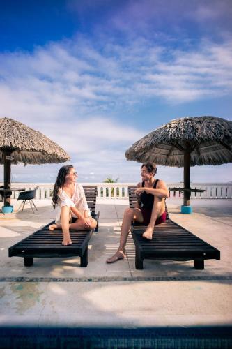 two people sitting on benches under an umbrella at Hotel Caracol Plaza in Puerto Escondido