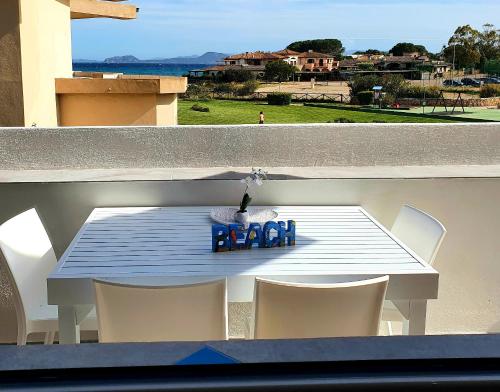une table avec des chaises blanches et un panneau bleu sur un balcon dans l'établissement Appartamenti delfini terza spiaggia, à Golfo Aranci