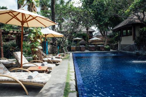 a pool with chairs and umbrellas next to a resort at Hotel Tugu Bali - CHSE Certified in Canggu