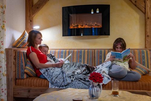 two women and a child sitting on a couch reading books at Almdorf Tirol in Haldensee