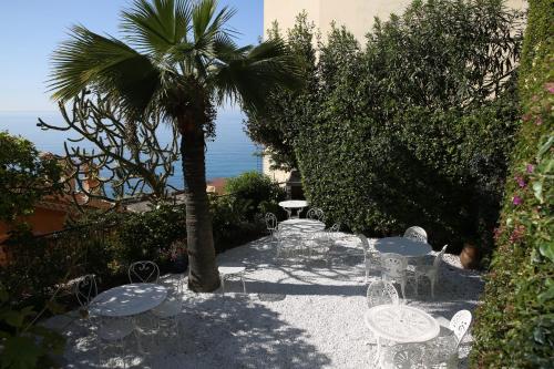 a patio with chairs and a palm tree and the ocean at Hotel de charme Regency in Roquebrune-Cap-Martin