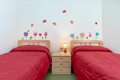two beds in a bedroom with red sheets and flowers on the wall at Casa Mincoti Piazza Terragnolo OSPITAR in Piazza