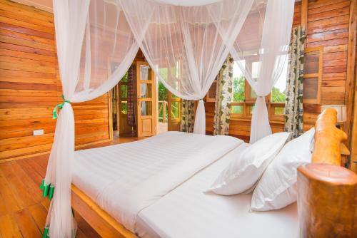 a bedroom with a white bed with white curtains at Engiri Game Lodge and Campsite in Katunguru