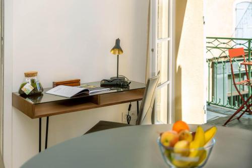 a bowl of fruit sitting on a table with a desk at Provence Au Coeur Appart Hotels in Forcalquier