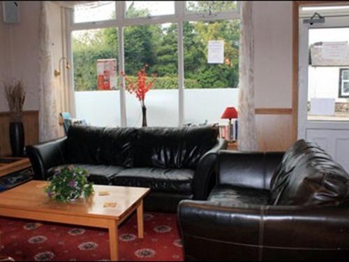 sala de estar con sofá de cuero negro y mesa en The Village Inn, en Kirtlebridge