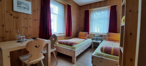 1 dormitorio con 2 camas, escritorio y mesa en Garni Alpenrose - Grusaida, en Scuol