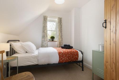 a bedroom with a bed with white sheets and a window at Holly Cottage in Ampney Crucis