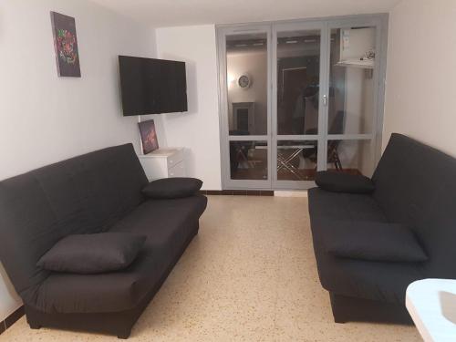 un salon avec deux canapés noirs et une télévision dans l'établissement Studio plage du môle, au Cap d'Agde