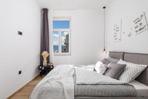 a white bedroom with a bed and a window at Apartment Vintasio in Rijeka