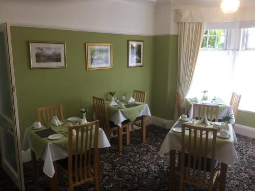 a dining room with tables and chairs with green walls at The Hilary Guest House in Llandudno