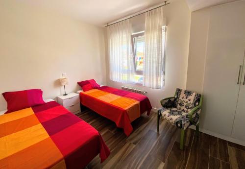 1 dormitorio con 2 camas, silla y ventana en Apartamentos Las Calas, en Santander