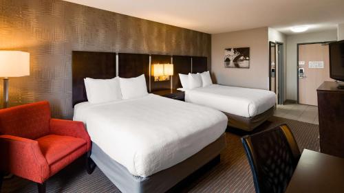 Cette chambre d'hôtel comprend deux lits et un fauteuil rouge. dans l'établissement Best Western Muscatine - Pearl City Hotel, à Muscatine