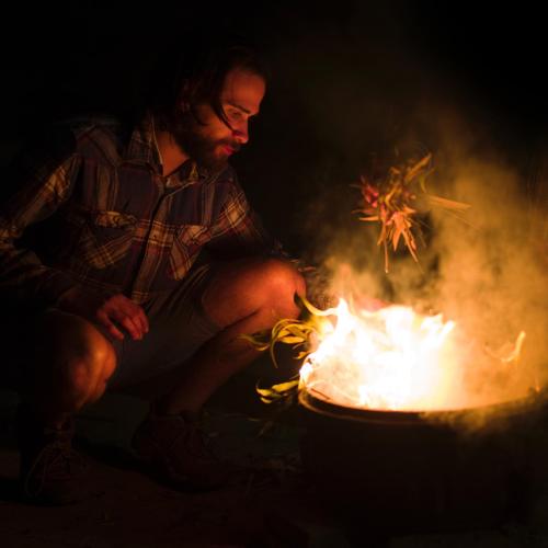 a man is sitting next to a bonfire at YHA Pittwater Eco, Sydney in Church Point