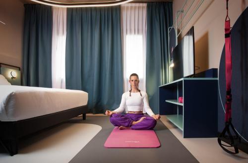 BrunelloにあるStay Hotelのベッド付きの部屋に敷物を敷いて座っている女性