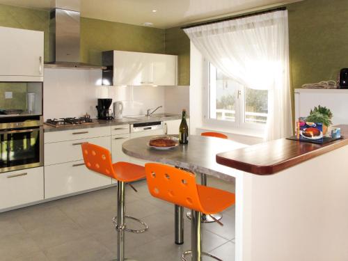Plounévez-LochristにあるHoliday Home Ty Thérèse - PLR205 by Interhomeのキッチン(白いキャビネット、オレンジの椅子付)