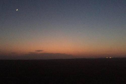 a sunset with the moon in the sky at cozy room in Mitzpe Ramon