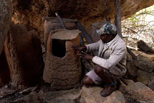 a man is sitting on a rock next to a small oven at Big Cave Camp in Matopos